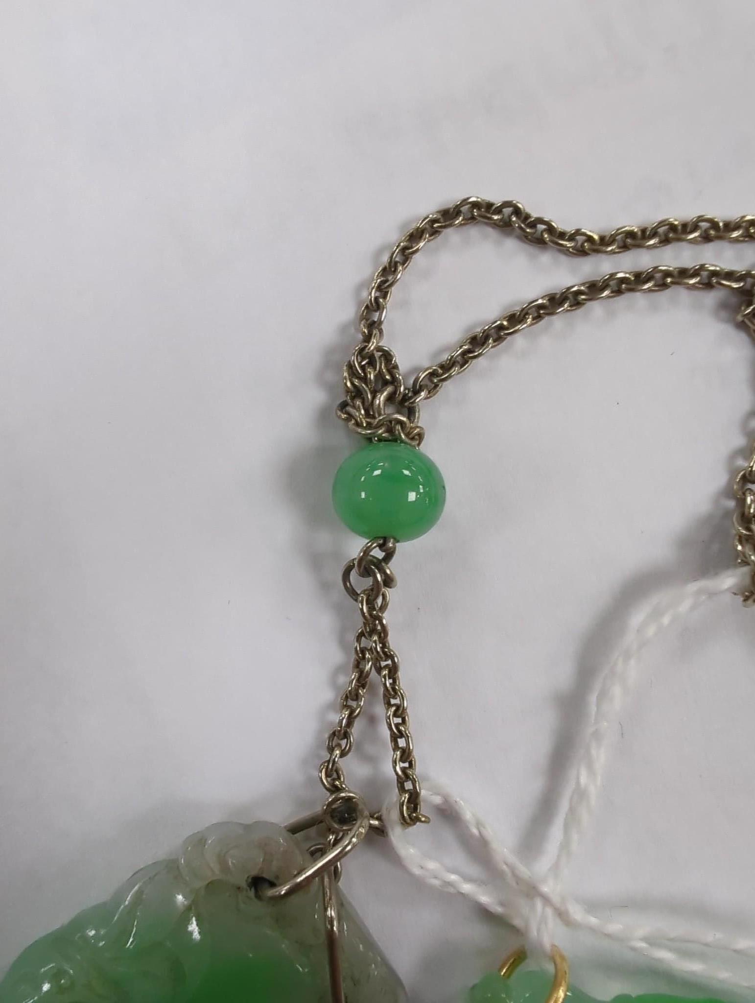 Two carved jade pendants, largest 47mm on a white metal chain.